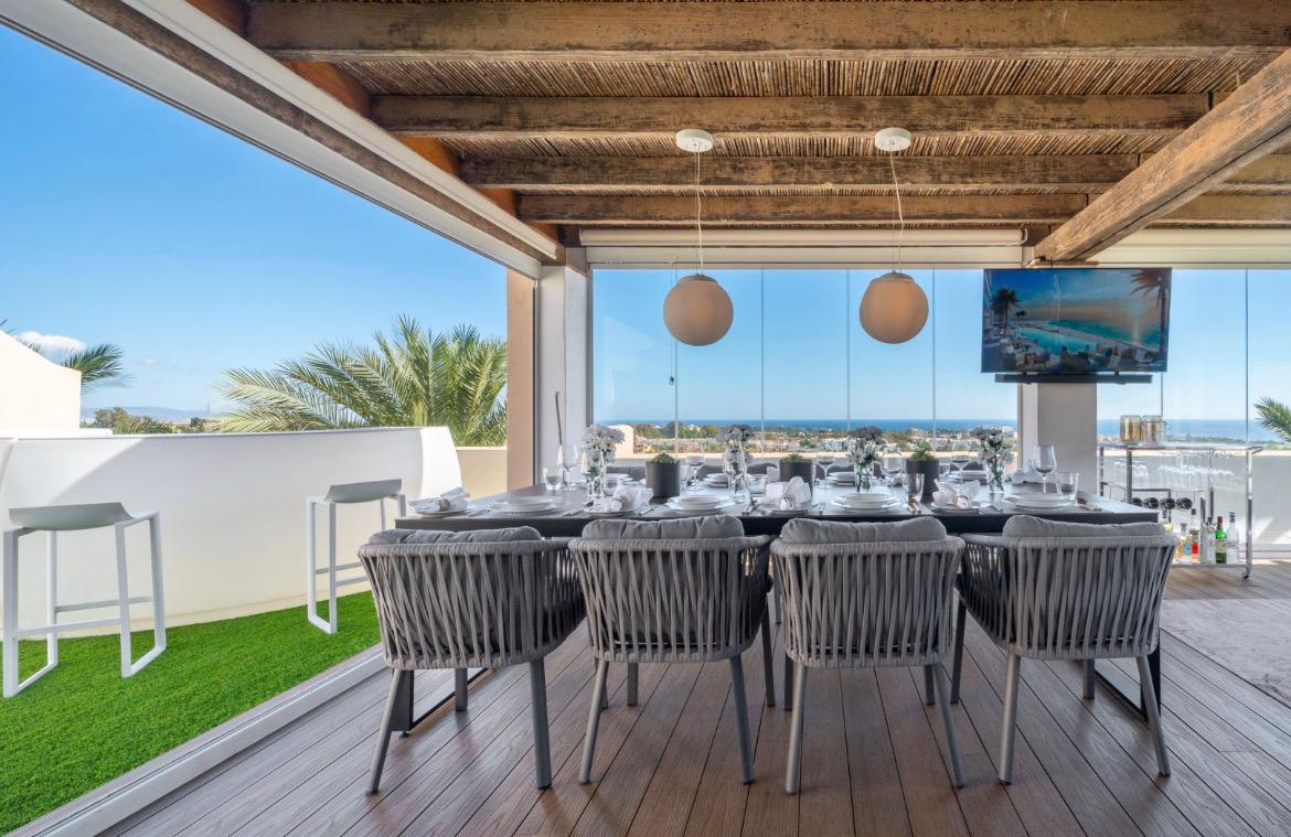 Glass-enclosed terrace dining with grey rope chairs and sea view