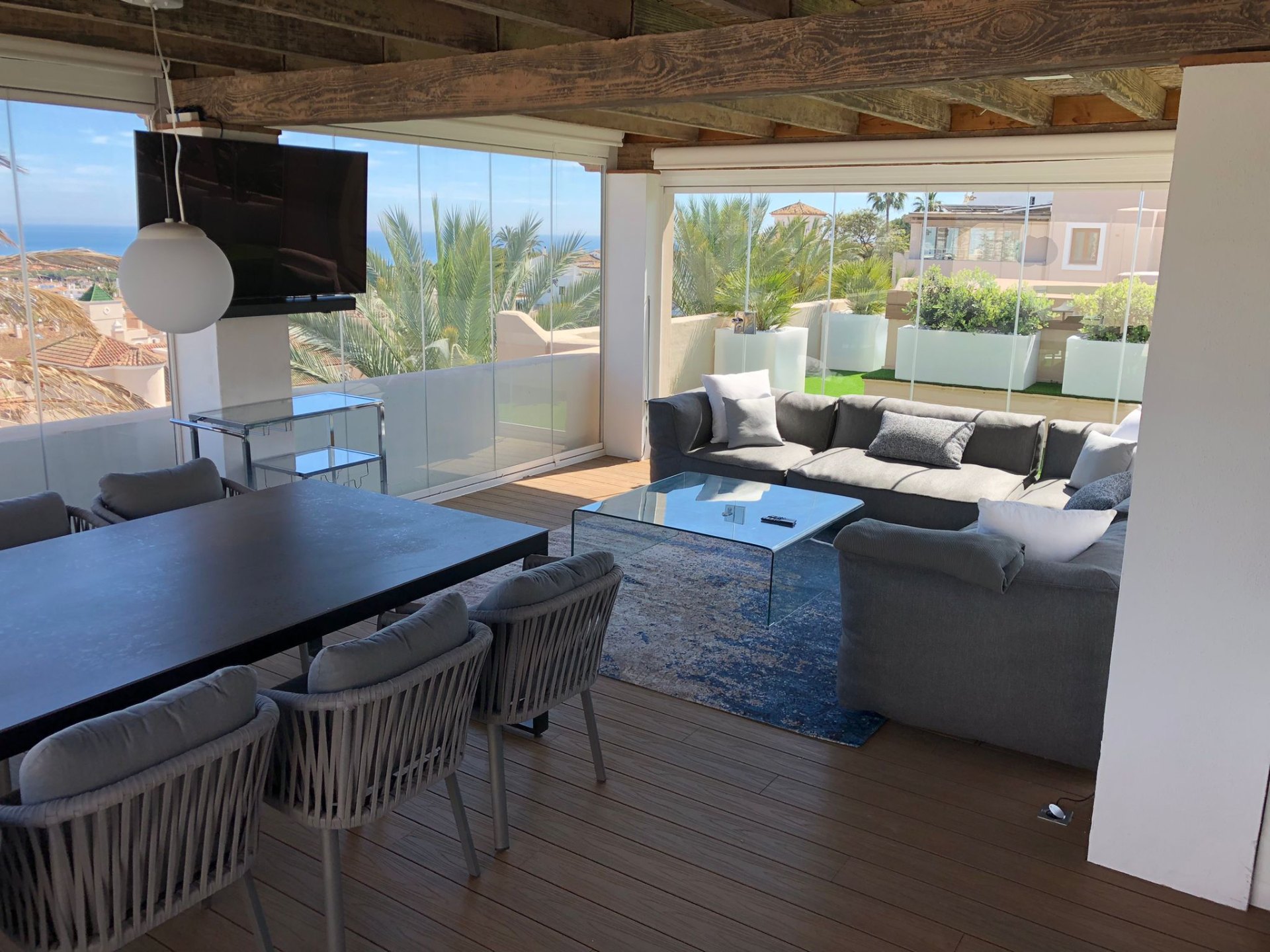 Glass-walled sunroom lounge with sea views and wood-beam ceiling